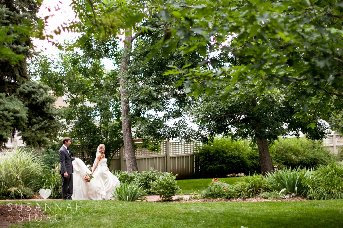 a wedding couple walk under green trees