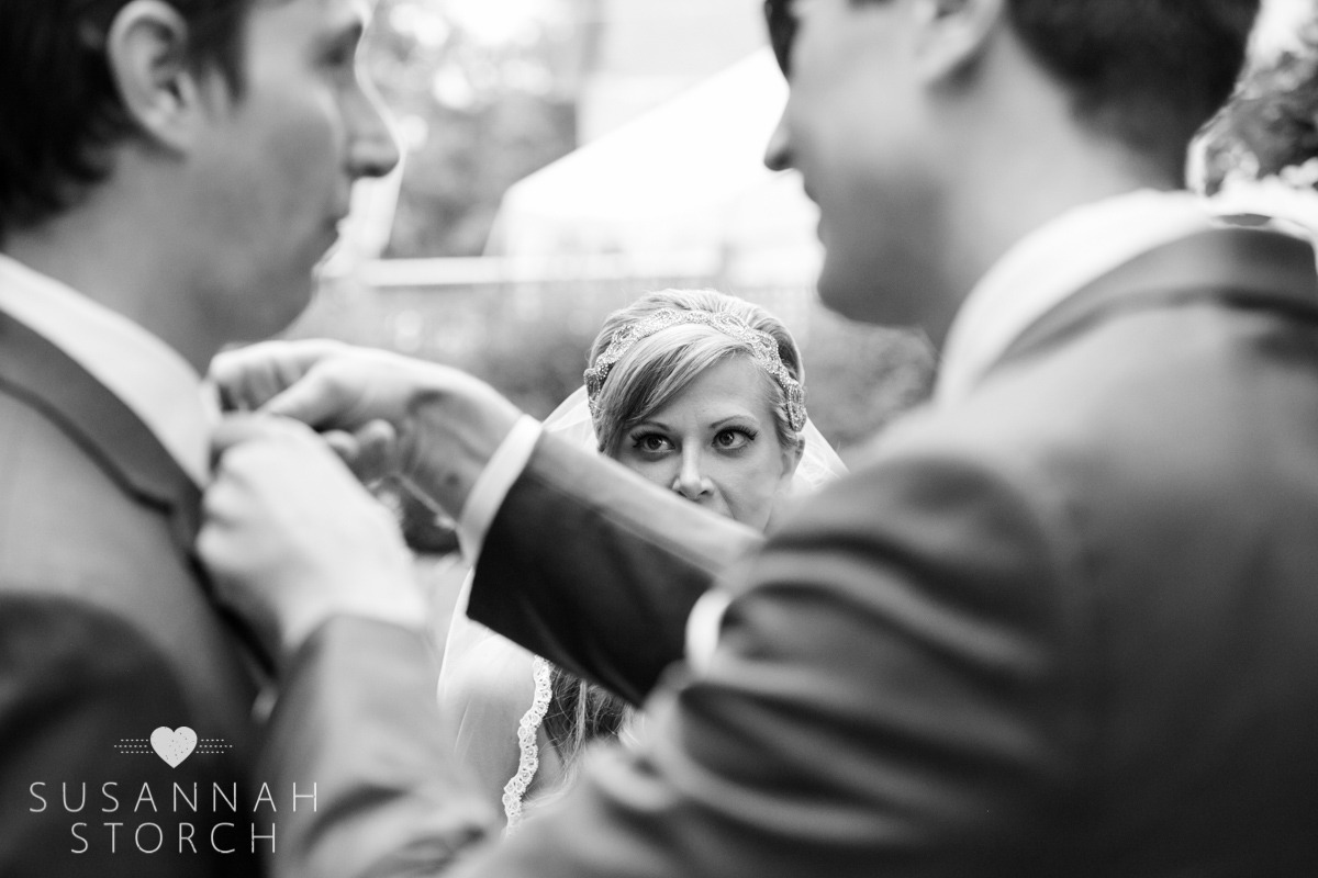a groomsman ties a bowtie under the watchful eyes of the bride