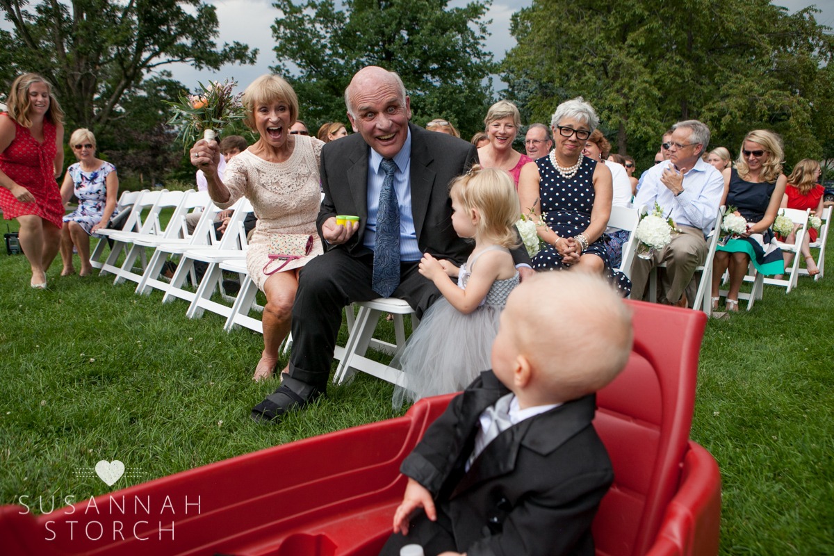 grandparents smile excitedly at the ring barer who rides in a red wagon