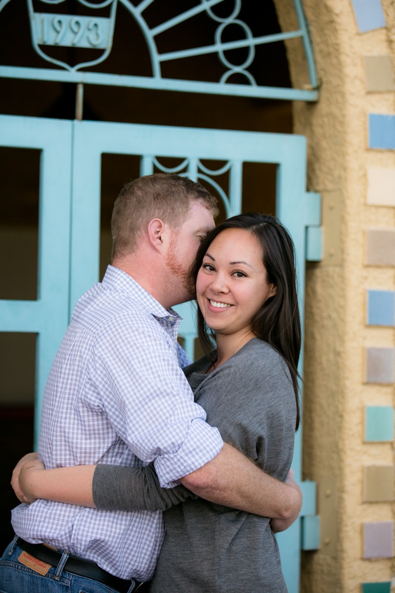 a man and woman embrace in front of a turquoise gate