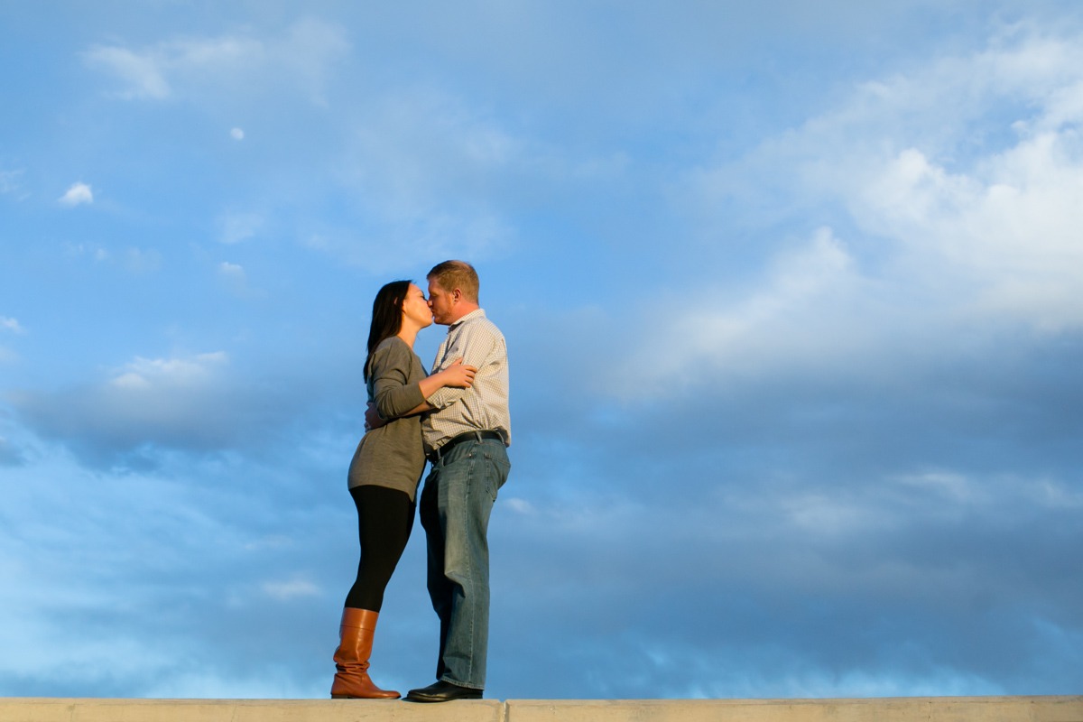 man and woman kiss in front of blue skies with clouds