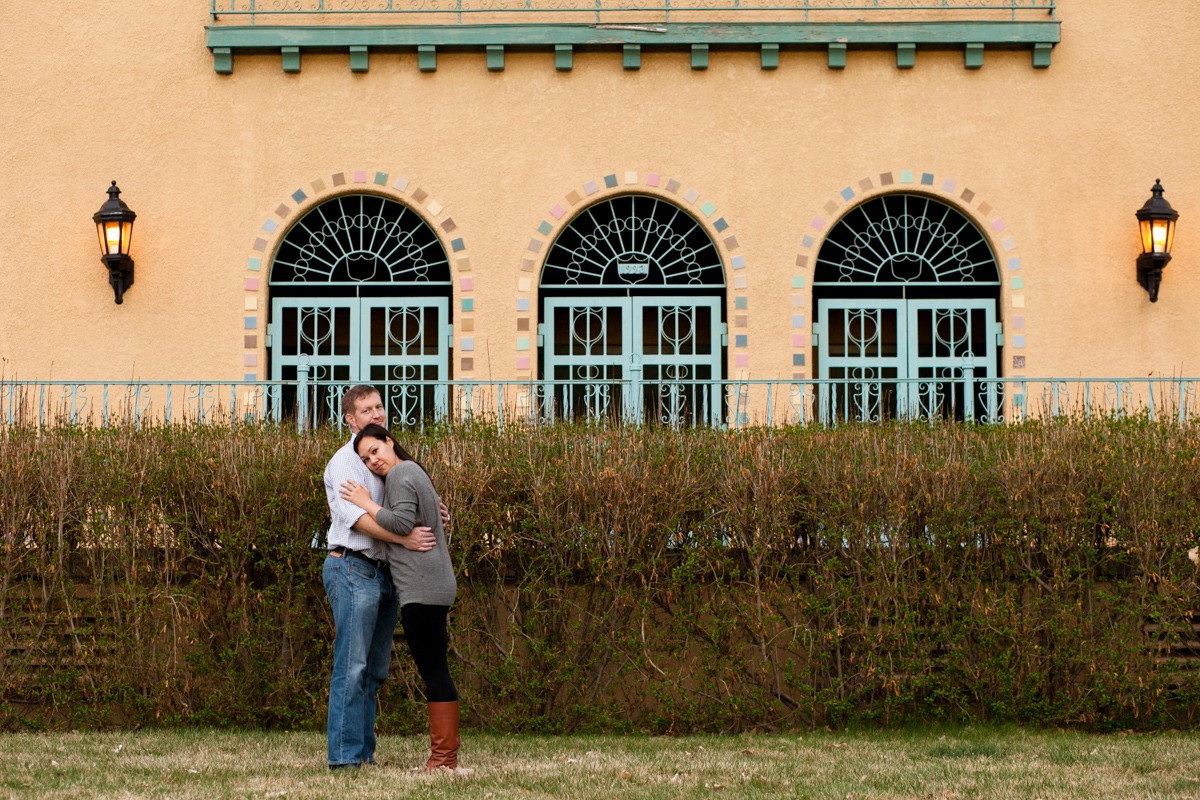 man and woman hug while standing in front of bushes and colorful arches