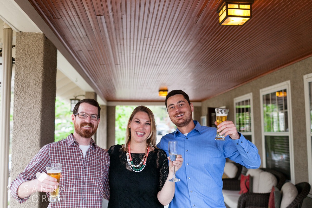 three wedding guests raise their drinks in a toast while standing on a porch