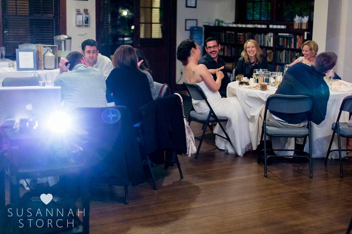 lingering guests sit at tables and laugh while a projector shines
