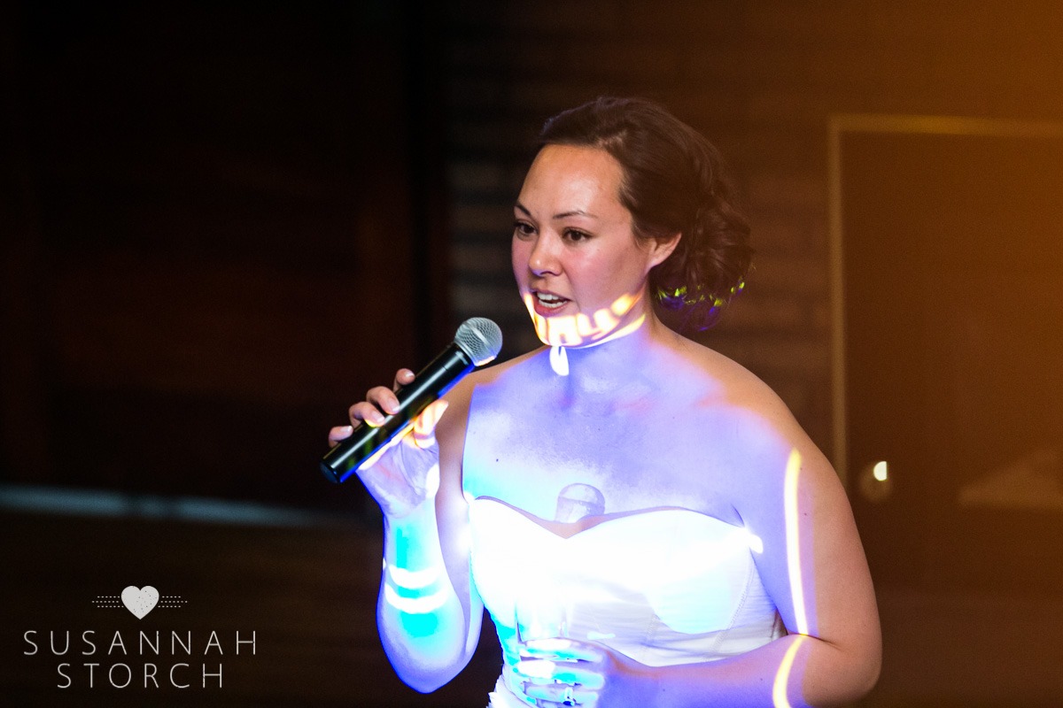 a bride holds a microphone while light from a screen is projected onto her