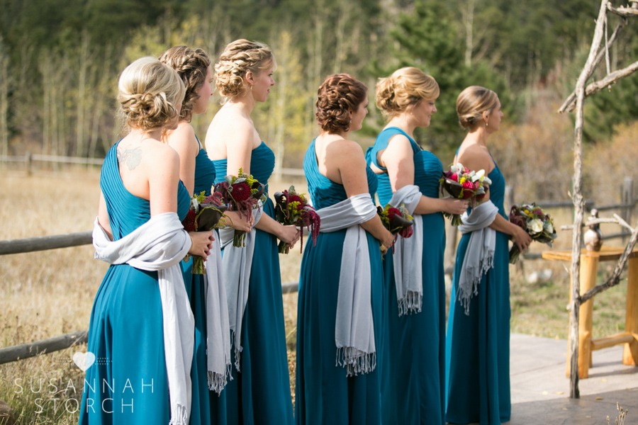 six bridesmaids wear teal dresses, light blue wraps, and hold burgundy bouquets