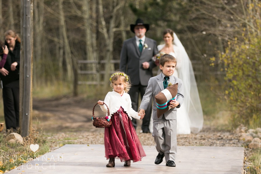 flower girl and ring bearer hold hands while walking down an aisle