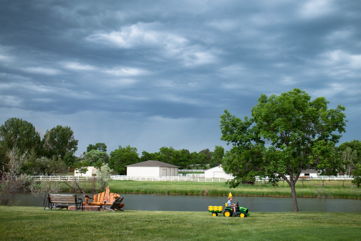 a boy drives a small tractor in front of a pond under stormy skies