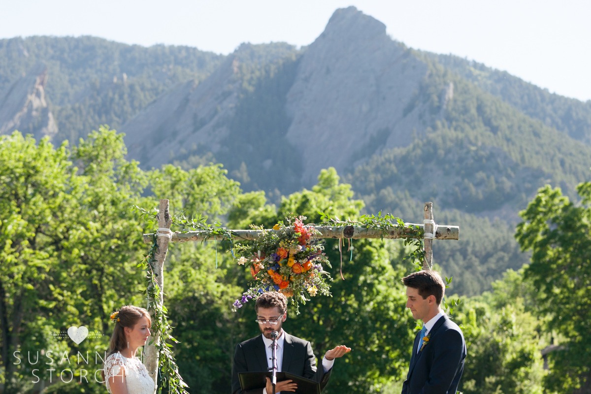an officiant raises his hands during a wedding in front of the flatirons