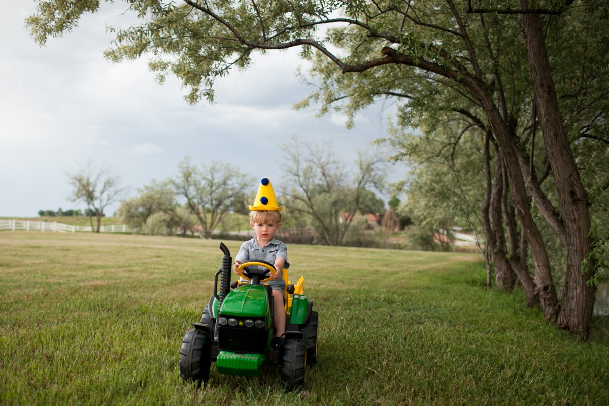 a boy in a yellow party hat drives a small tractor