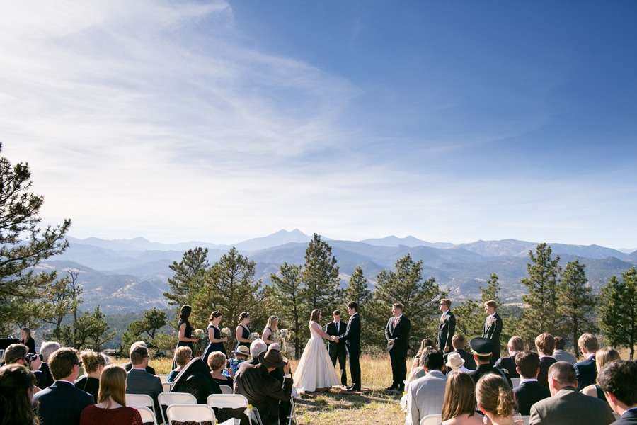 a bride and groom hold hands during their wedding ceremony with longs peak in the background