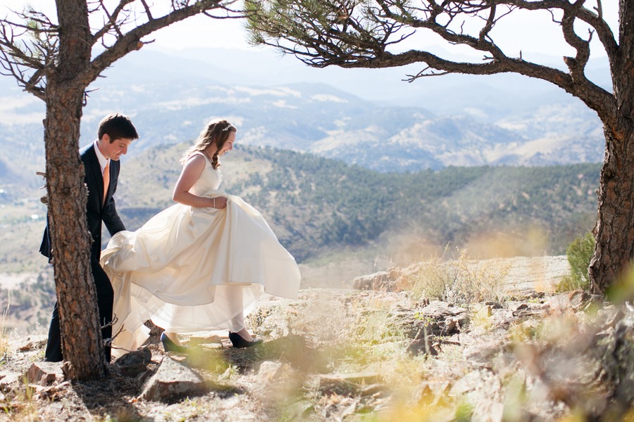 a bride walks in front of a mountain and valley while her new husband helps