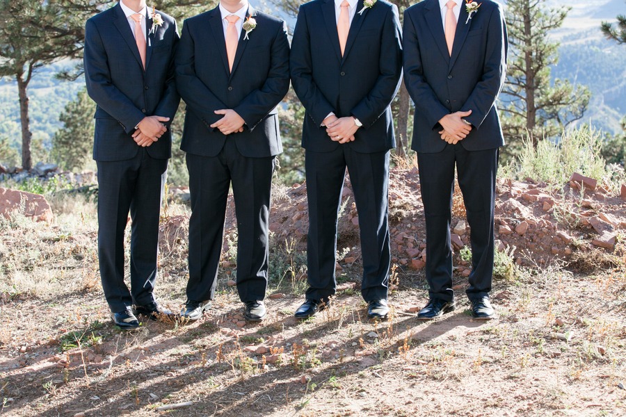 four men in suits stand in a row with their hands crossed