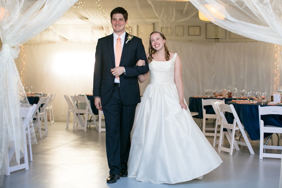 a bride in a cream gown and a groom with a peach tie walk into their wedding reception