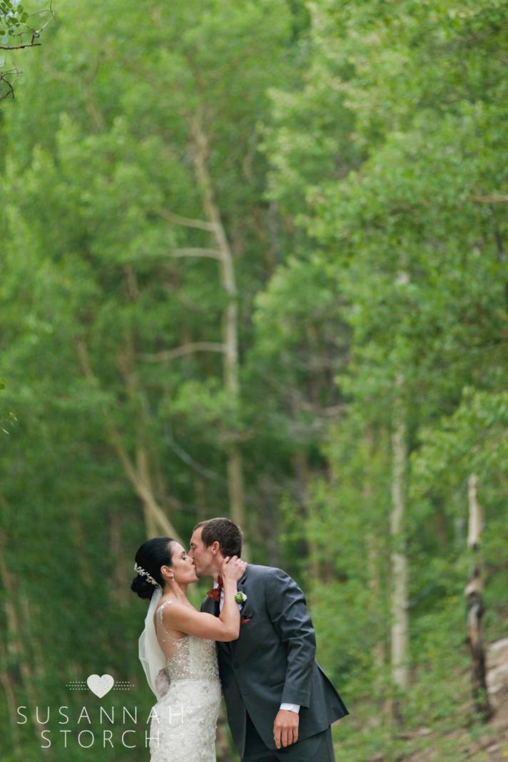 a wedding couple kiss in front of green trees