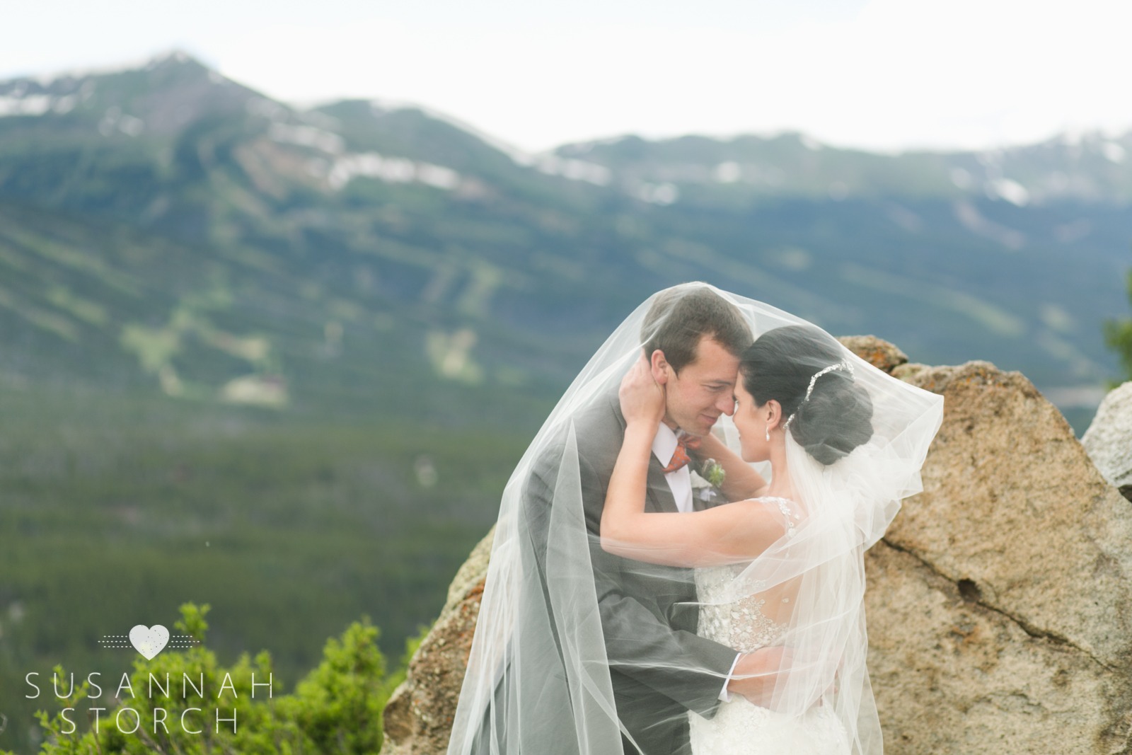 a wedding couple look at each other under a long veil in front of a ski resort