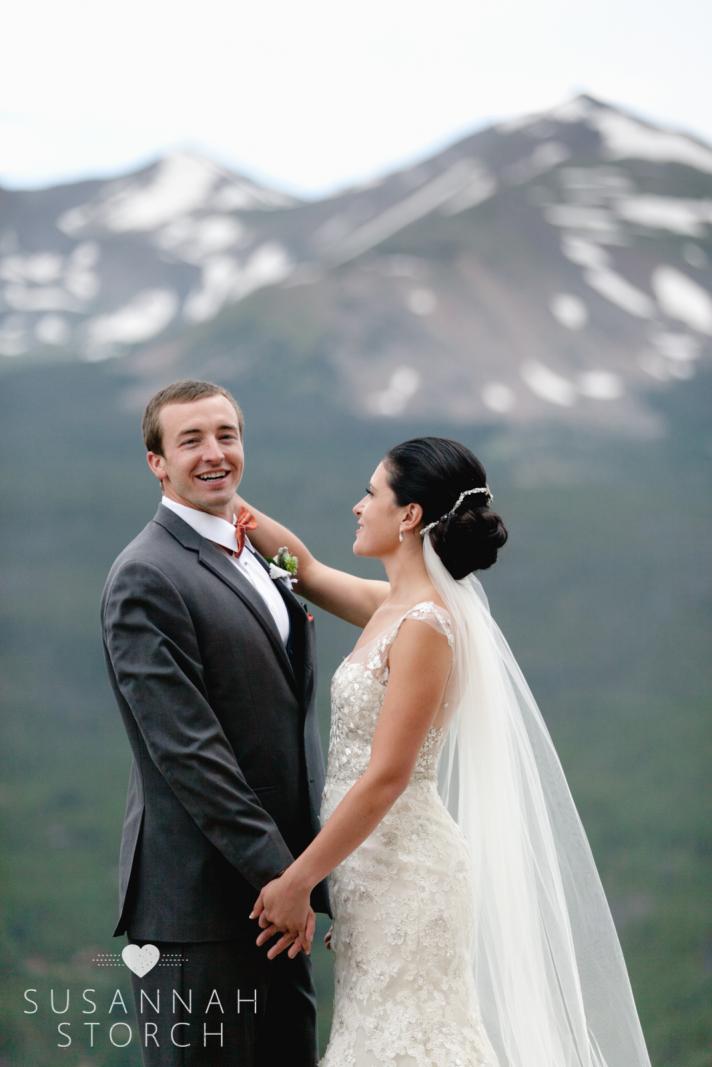a bride grooms her groom in front of snowy mountains