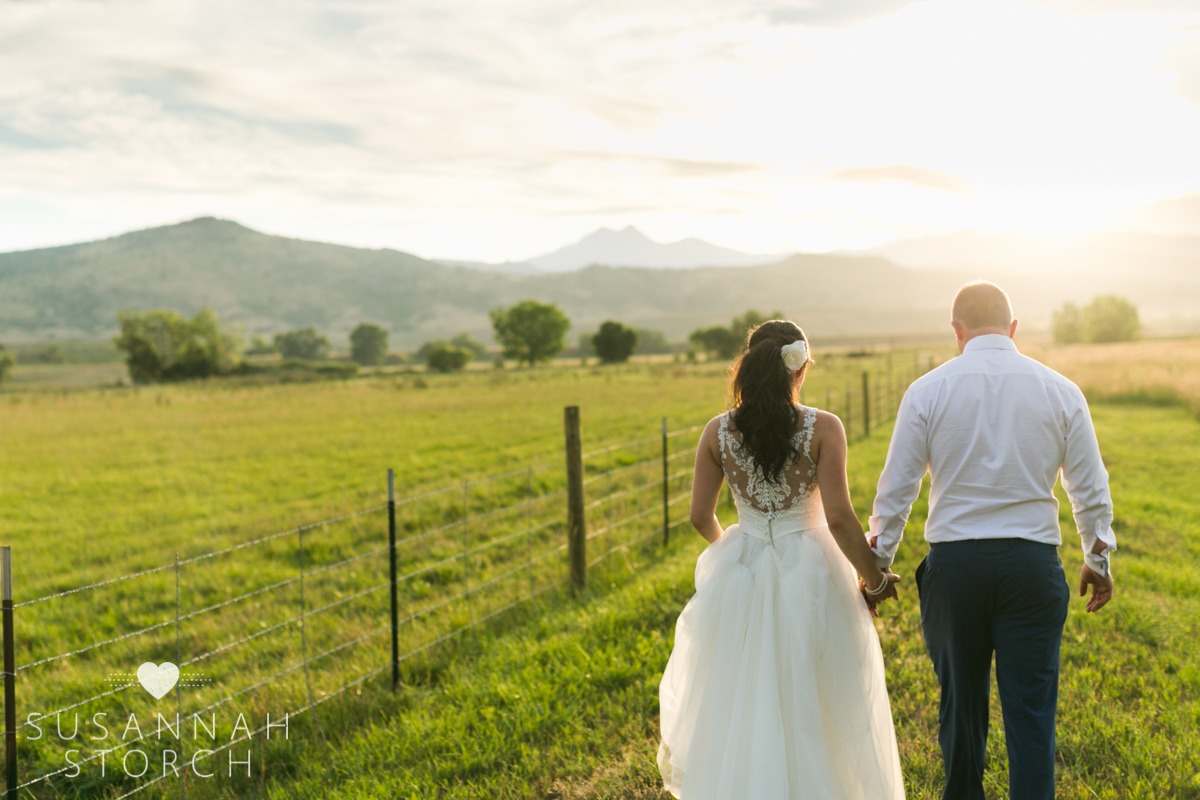 a bride and groom holds hands while walking into a sunset