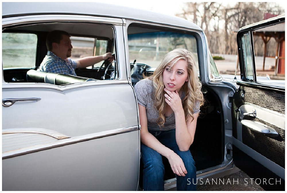 a blonde woman leans out of an older gray car