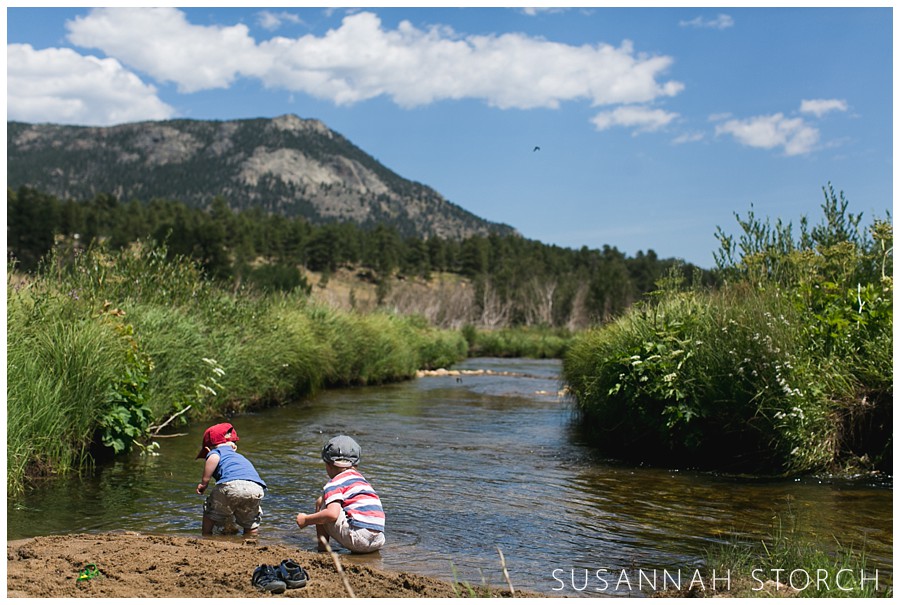two young boys squat down by a mountain stream