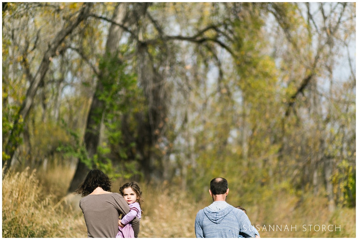 a family walks away from the camera with the girl looking back