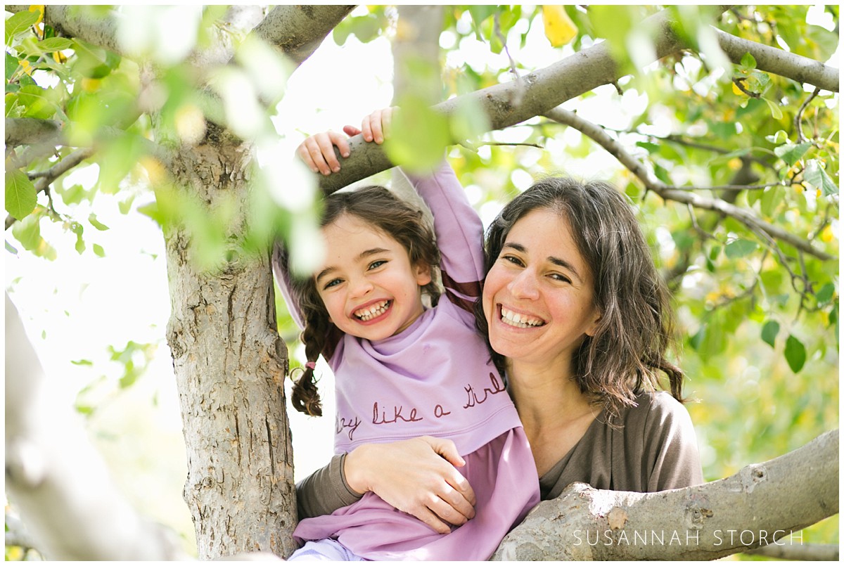 a mom and daughter smile while hanging out in a tree
