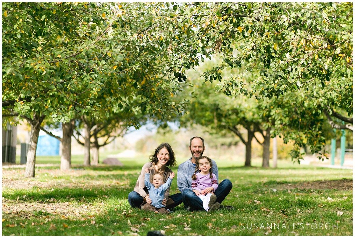 a family sits in front of two rows of apple trees