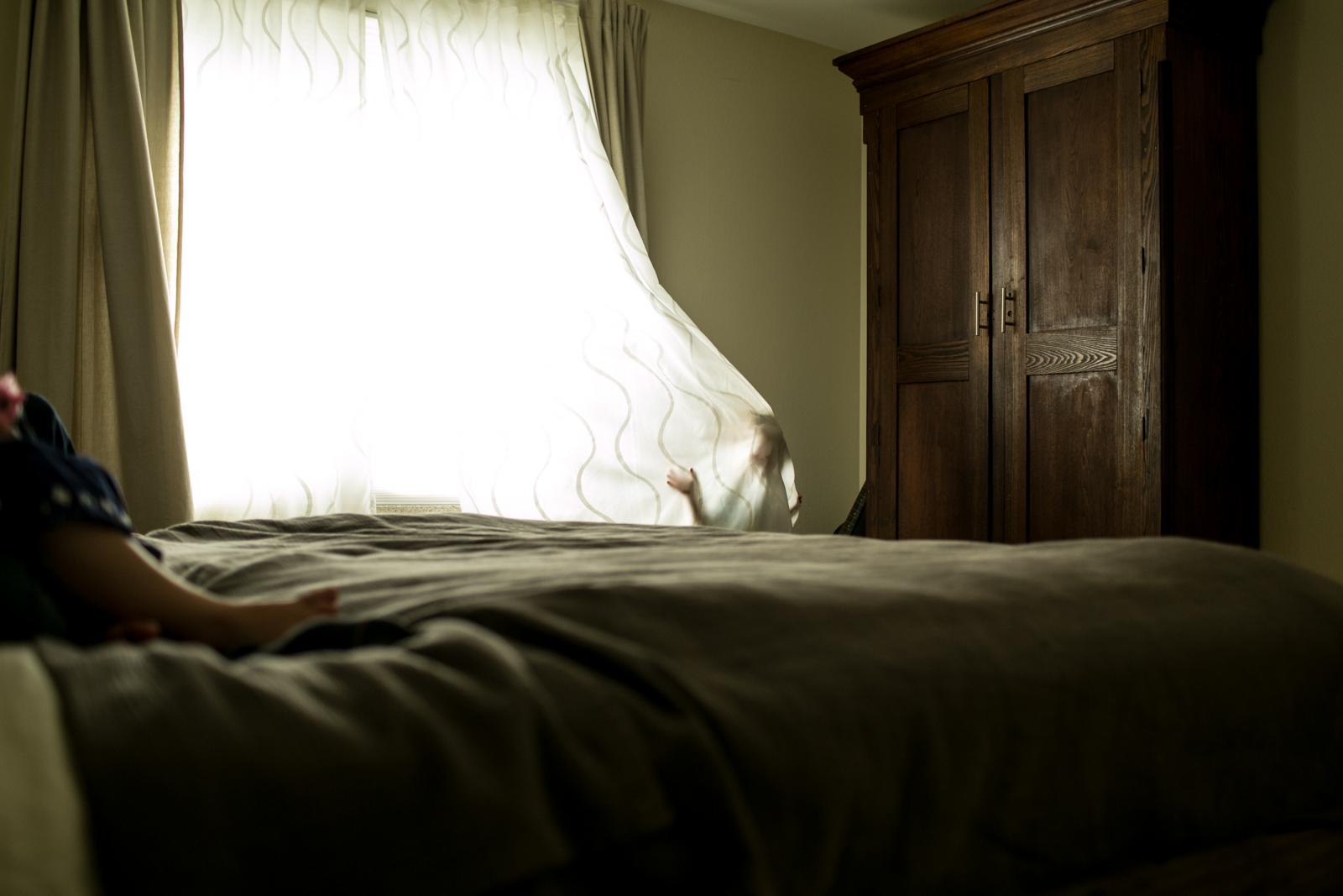 a boy reaches out from behind shear curtains during an in home photography session