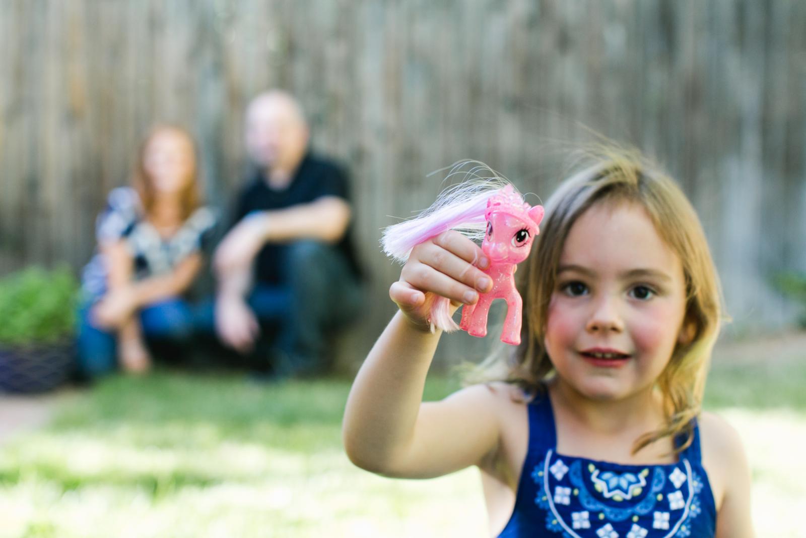 Boulder County in-home family photography session with a girl holding a toy to the camera in her backyard