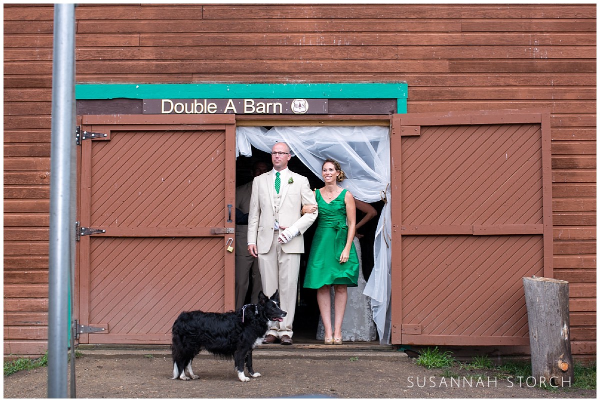 a bridesmaid and groomsman wearing green accents are about to exit a red barn