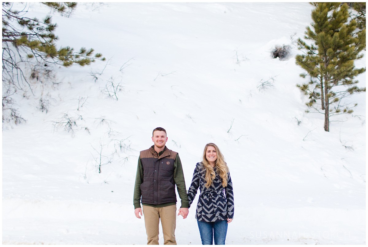 a man and woman hold hands in front of a wall of snow