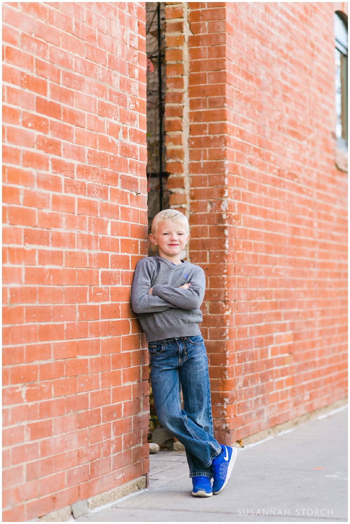 a boy leans on a brick wall