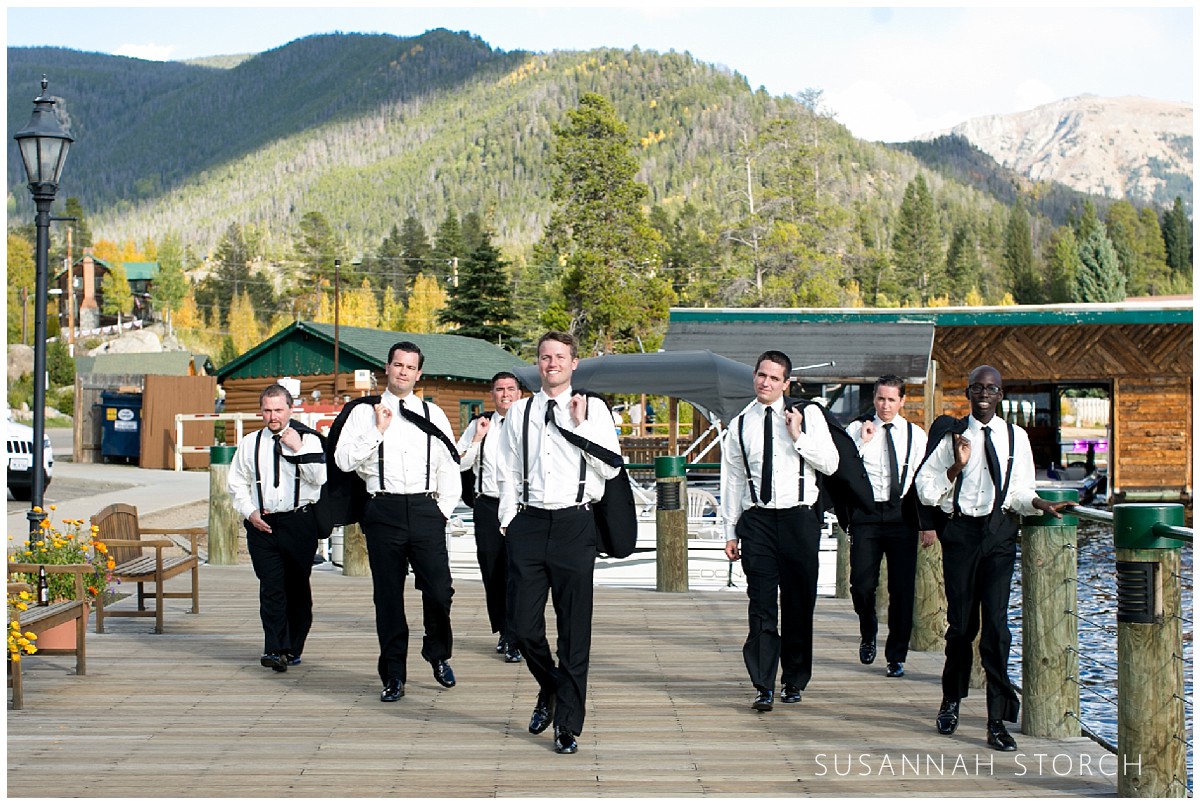 a group of men in suits walk on a pier at a mountain lake