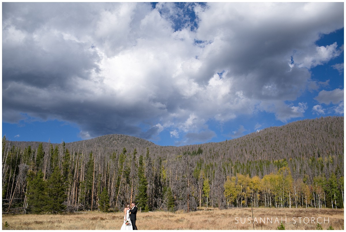 a bride and groom kiss under dramatic clouds