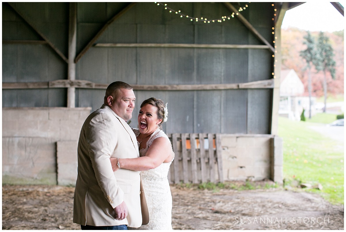 a bride laughs and hugs her groom in a barn