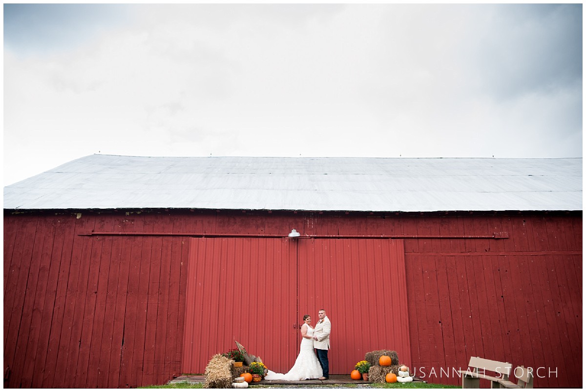 a bride and groom stand in front of a red barn