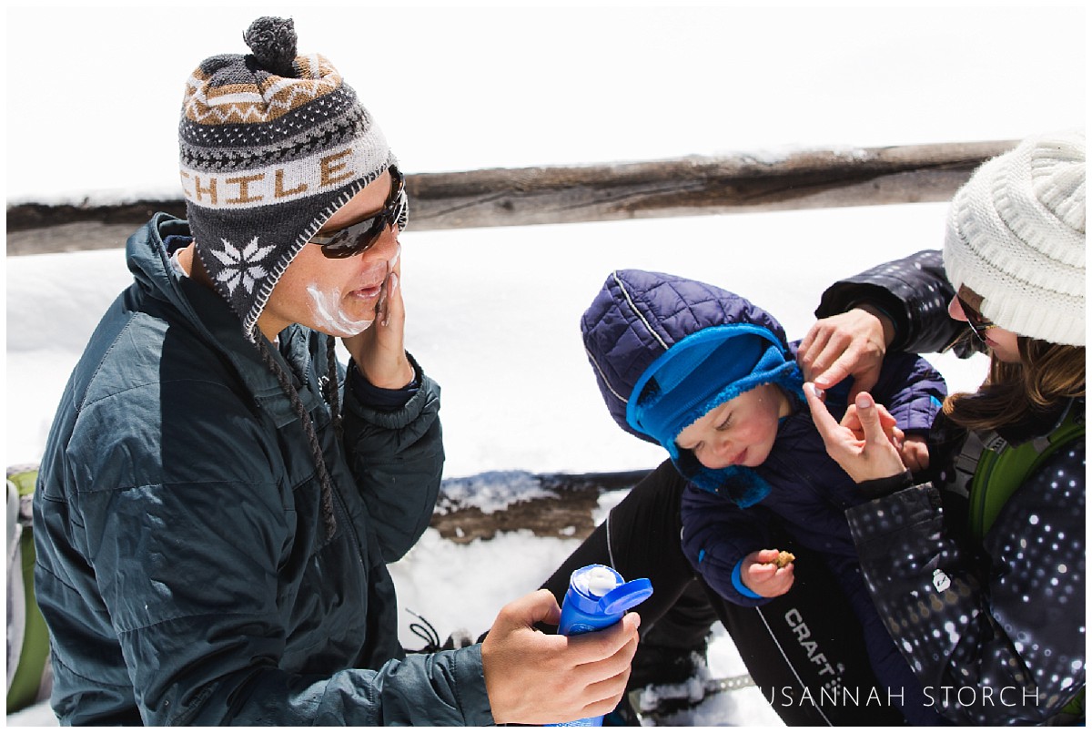 a dad slathers sunscreen on his face on a snowy day