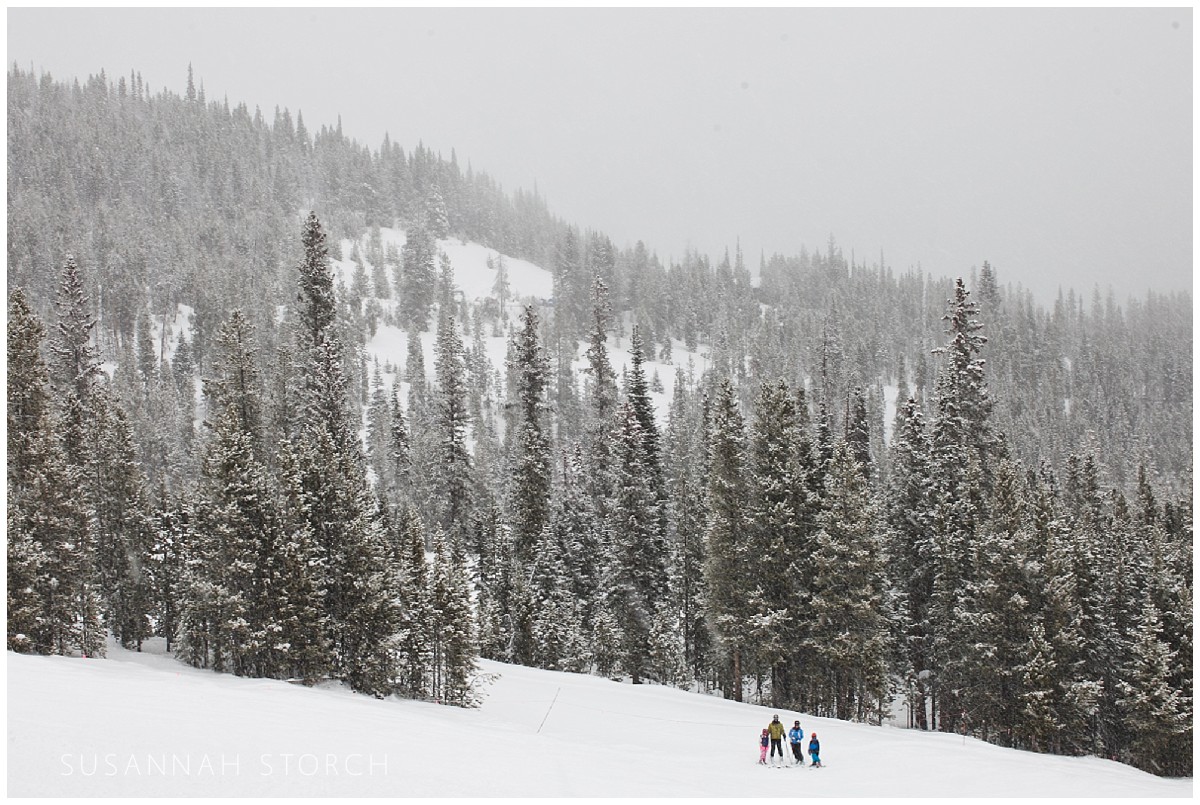 a family stands among snowy pinetrees