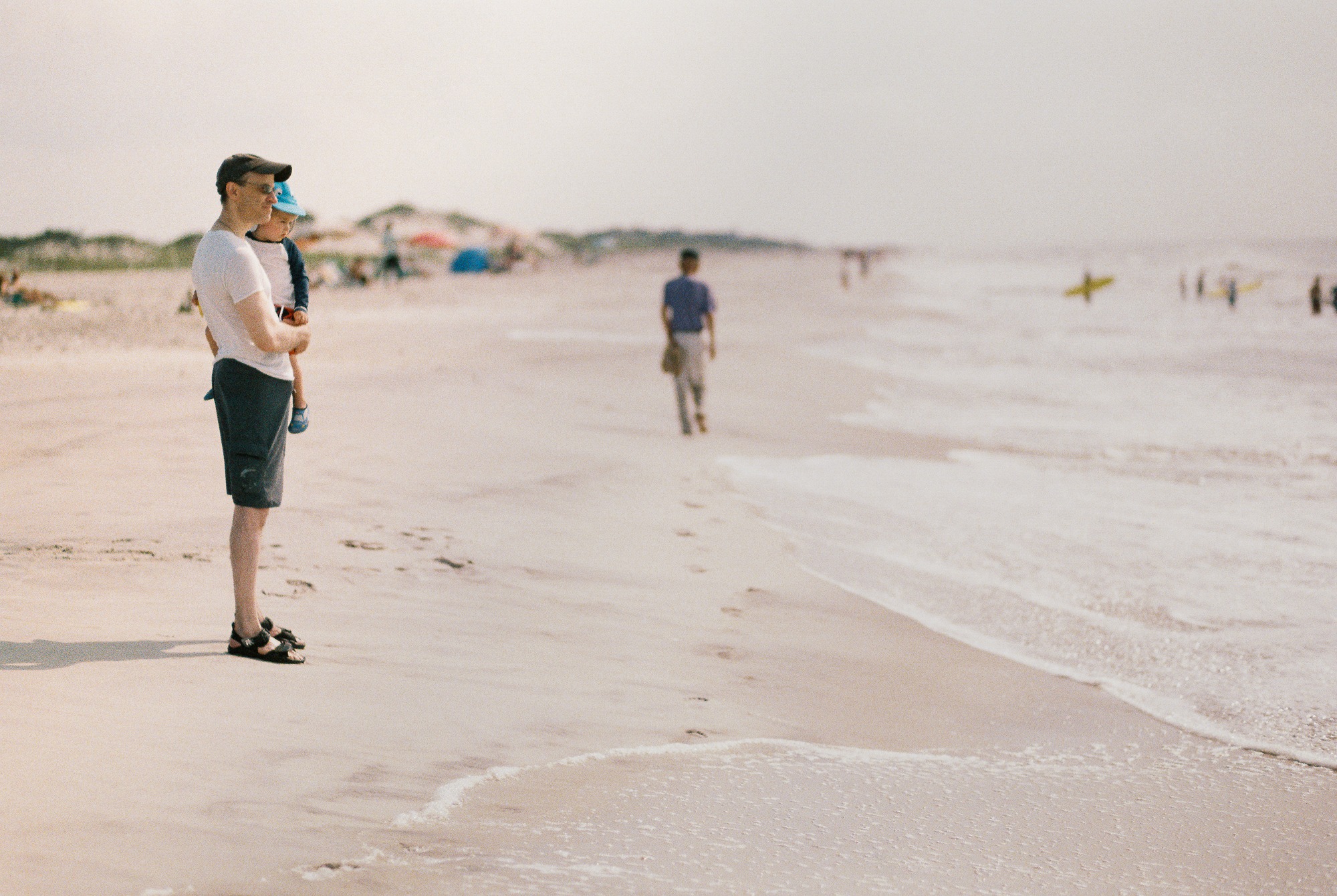 A man and his young son look out towards the ocean in a film photograph taken at Fire Island, NY