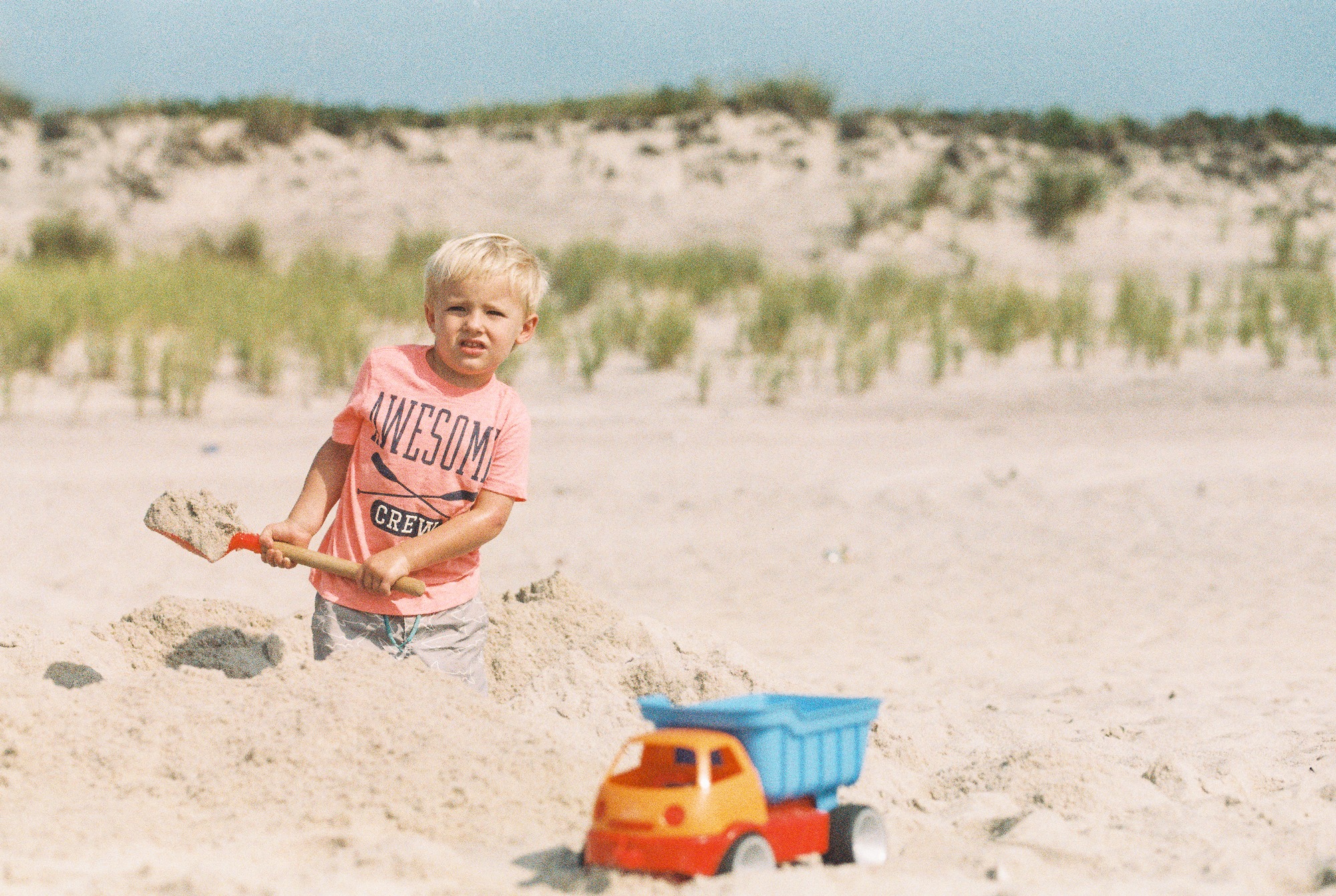 a boy digs in the sand in this image taken with expired film on fire island, ny