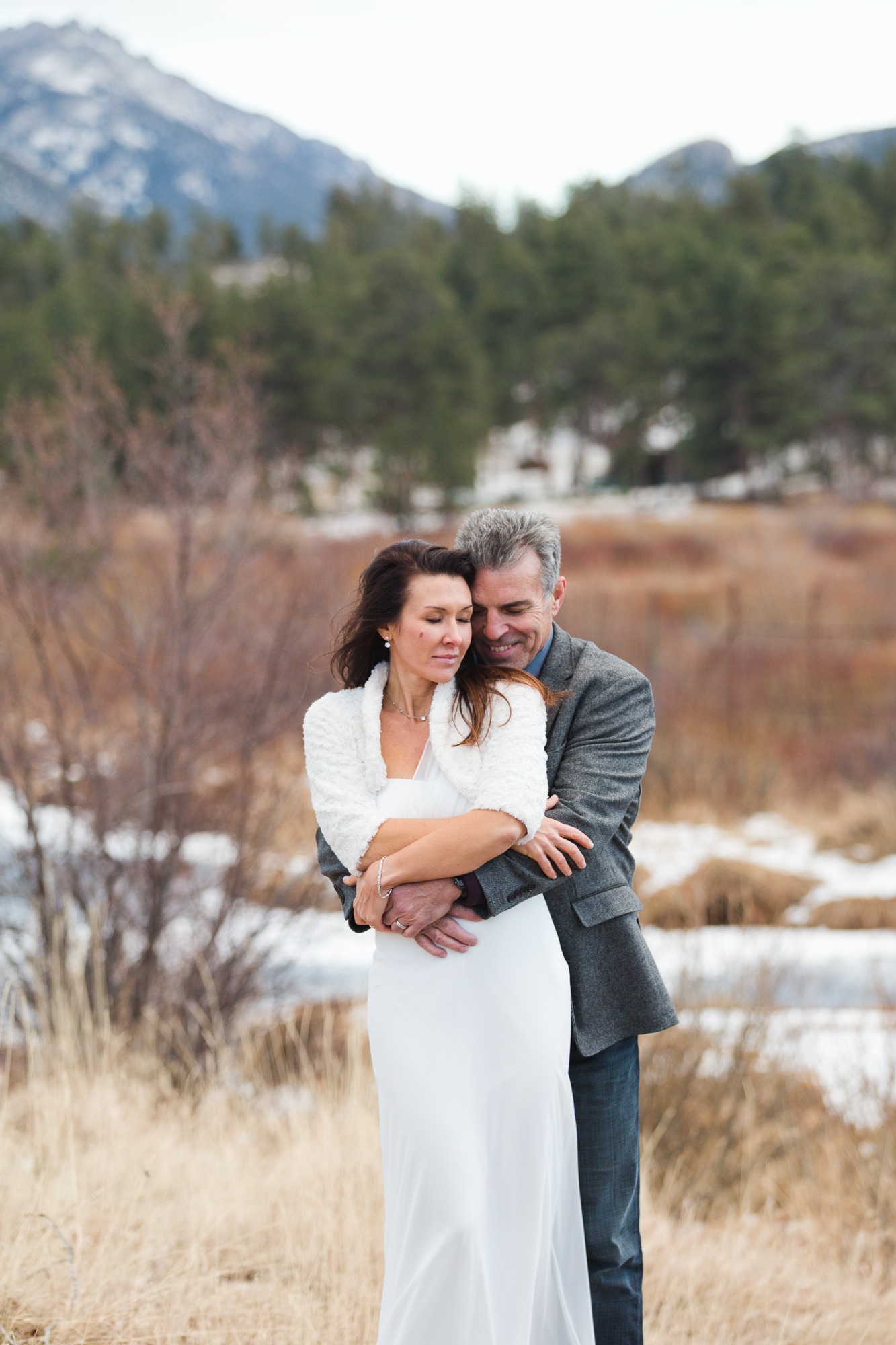 A married couple pose for a portrait in Rocky Mountain National Park in front of willows on a winter day.