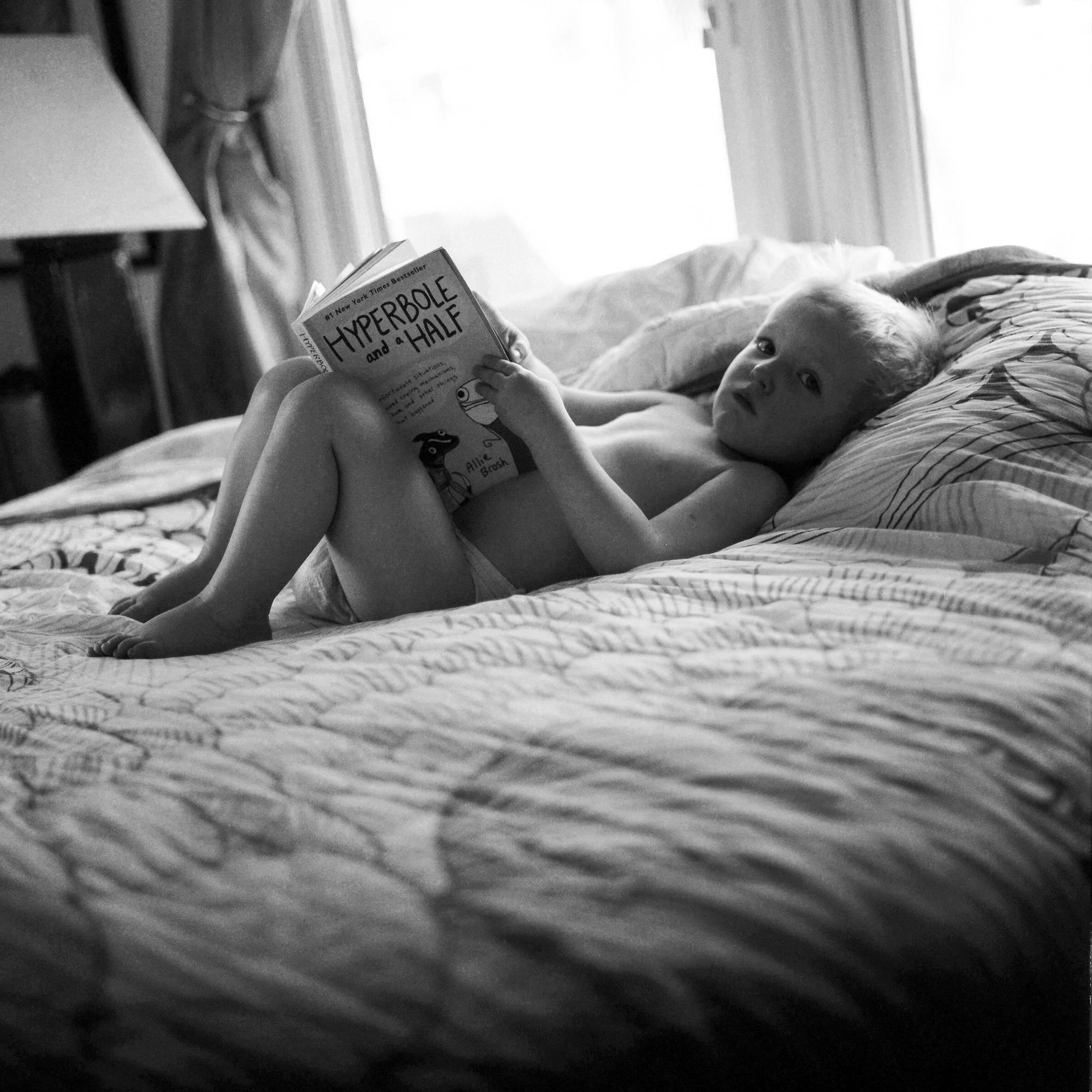 black and white film photograph of a boy reading a book on a bed