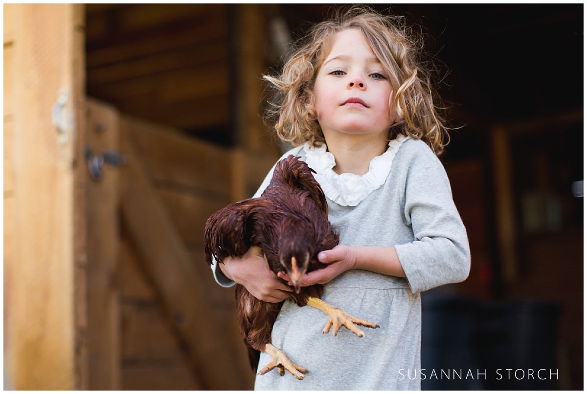 a young girl defiantly holding a brown chicken