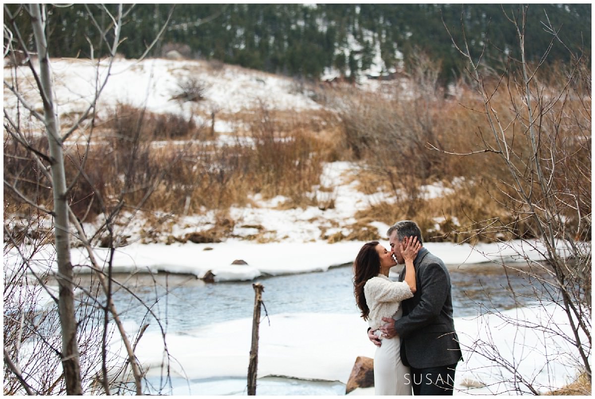 a couple kiss in front of a small river in rocky mountain national park
