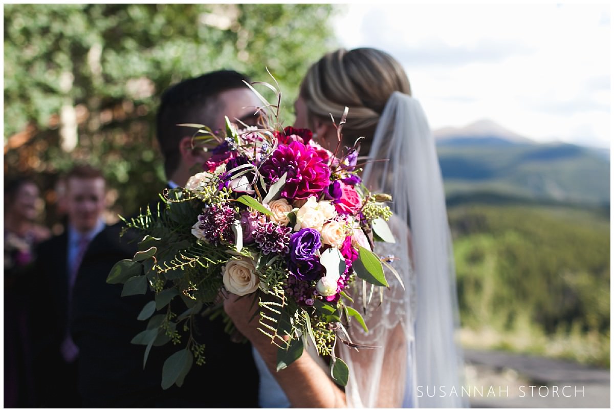 a bride and groom kiss behind a bouquet