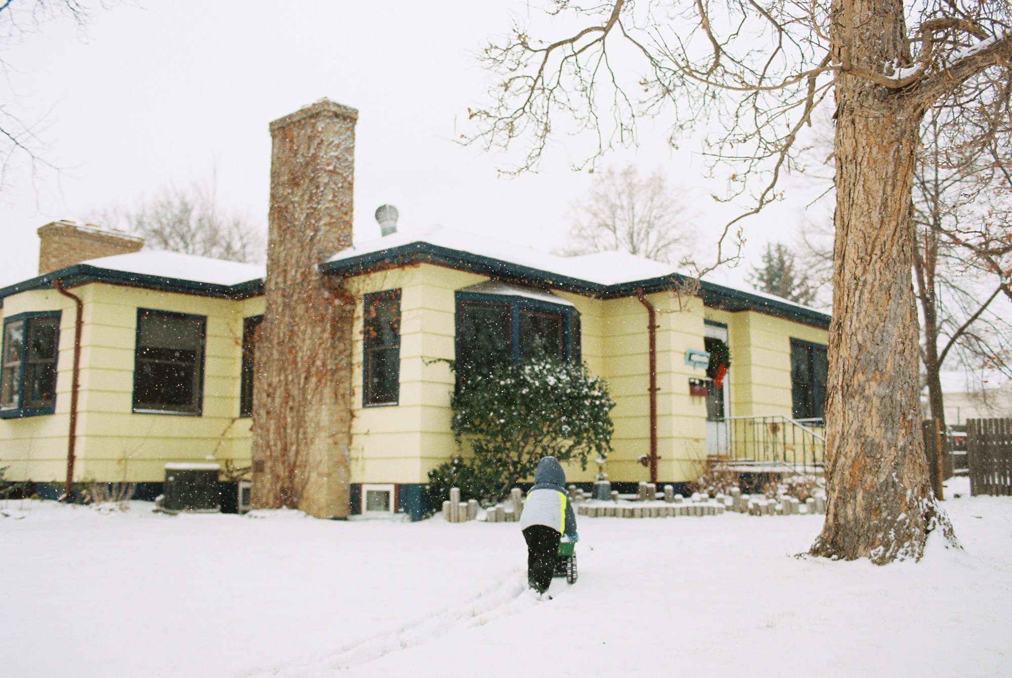 a boy walking towards a yellow house in the snow