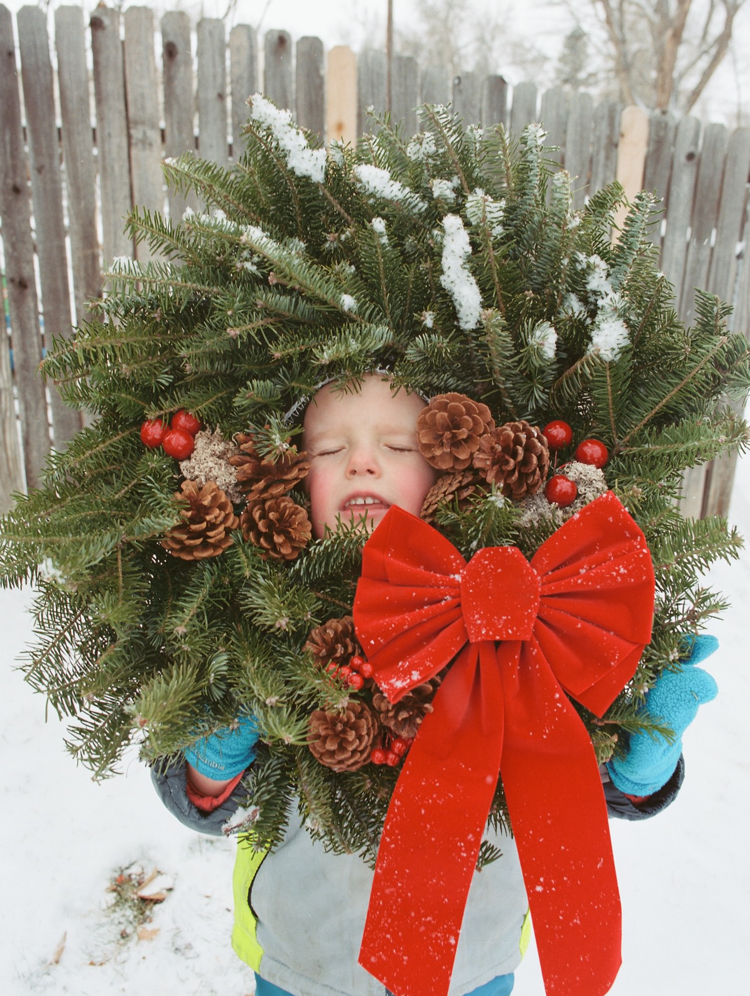a colorado boy sticks his head in the center of a christmas wreath