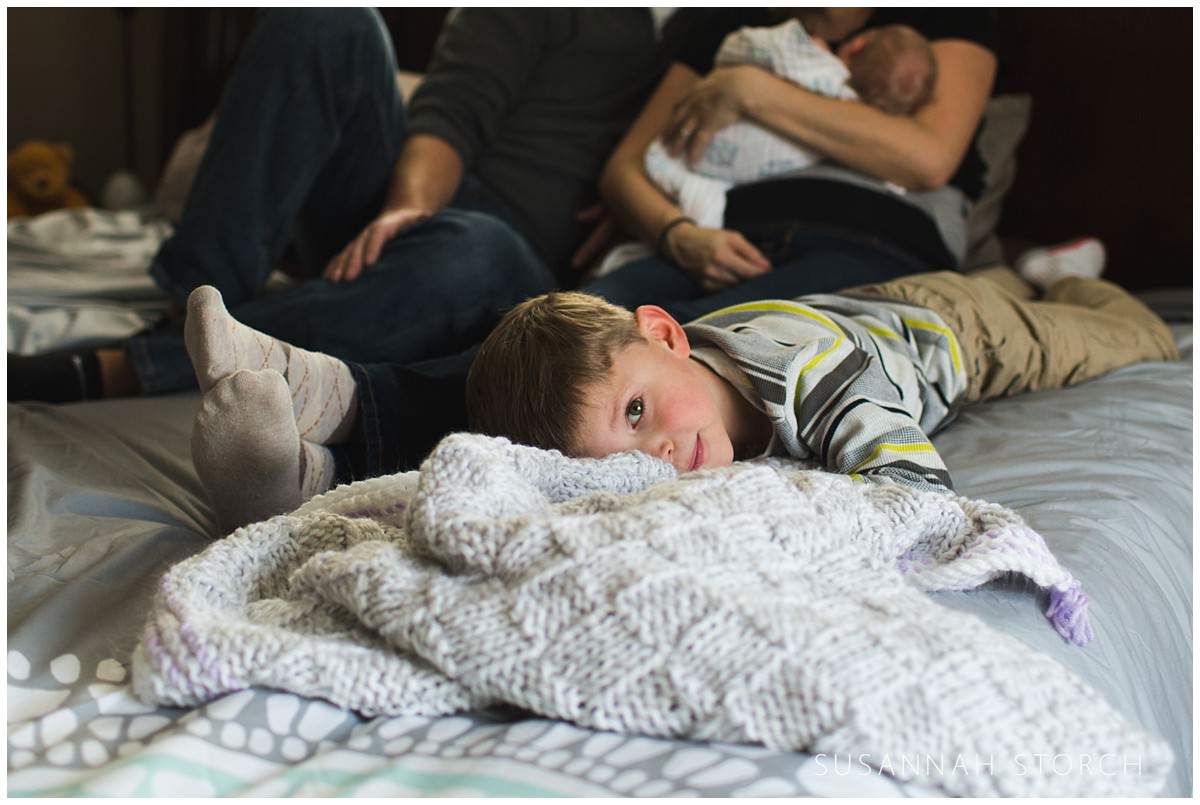a boy looks at the camera as he family lies on a bed behind him
