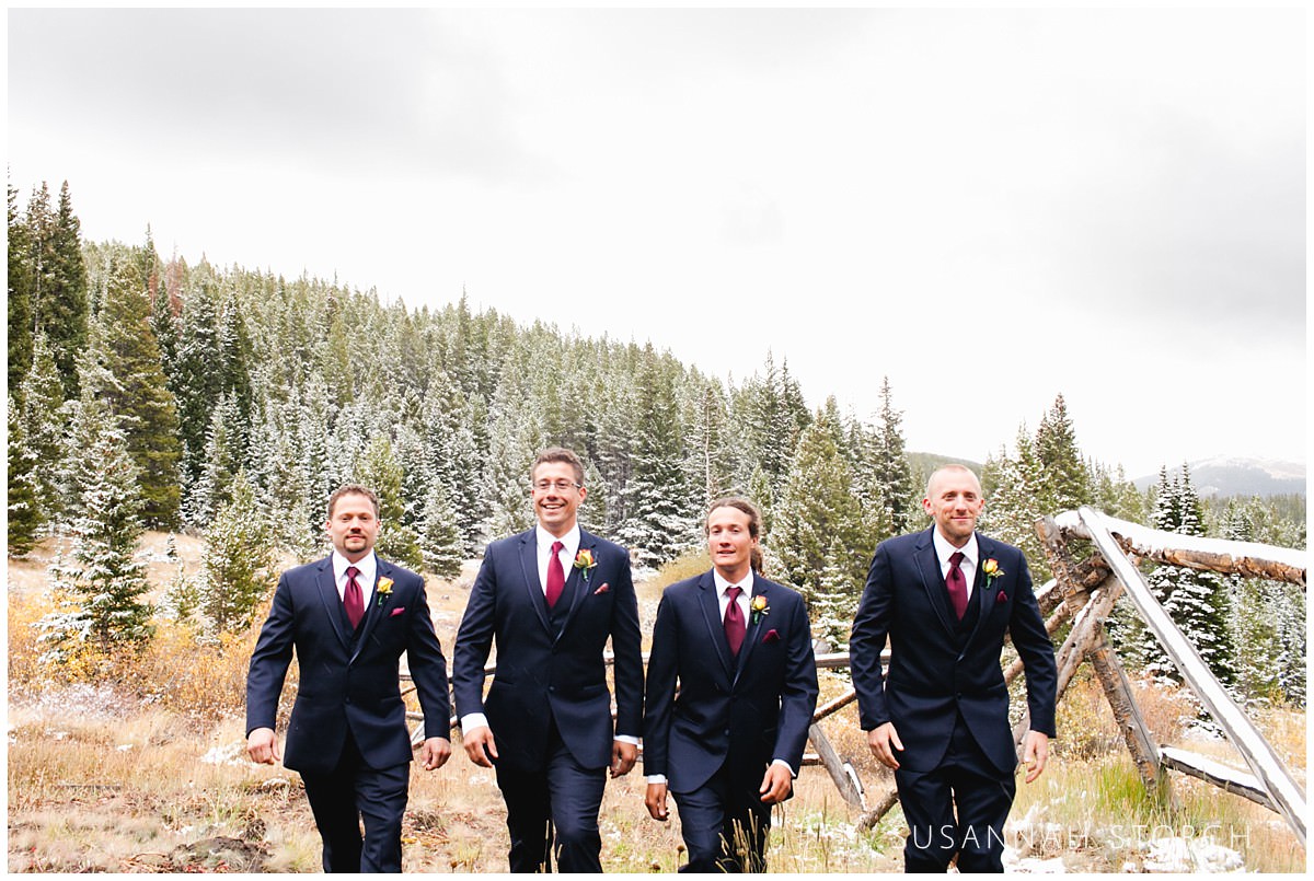 four men walk in front of snowy pine trees
