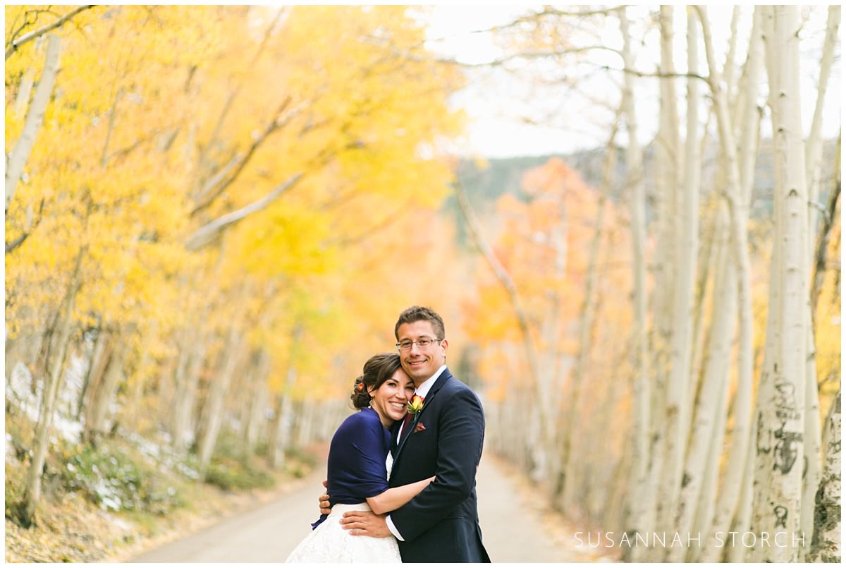 a bride and groom stand in a dirt road surrounded by fall trees